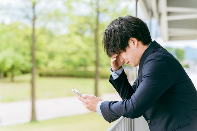 携帯を持ちながら悩む男性